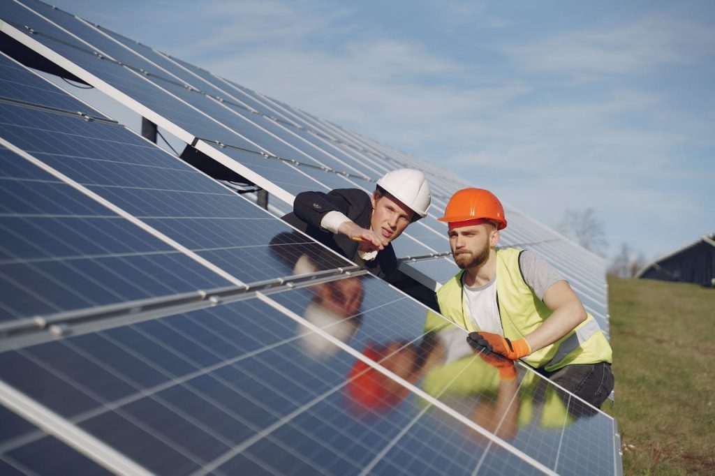 electricians-inspecting-the-solar-panels-4254162 Concentrated male coworkers in hardhats working at solar energy station and discussing technical aspects of panels